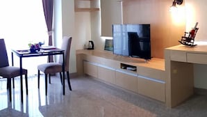 A modern living room with a flat-screen TV, a dining area with a table and chairs, and a kitchen area with a microwave and a coffee maker. - The Route Sriracha Hotel And Residence (Si Racha)