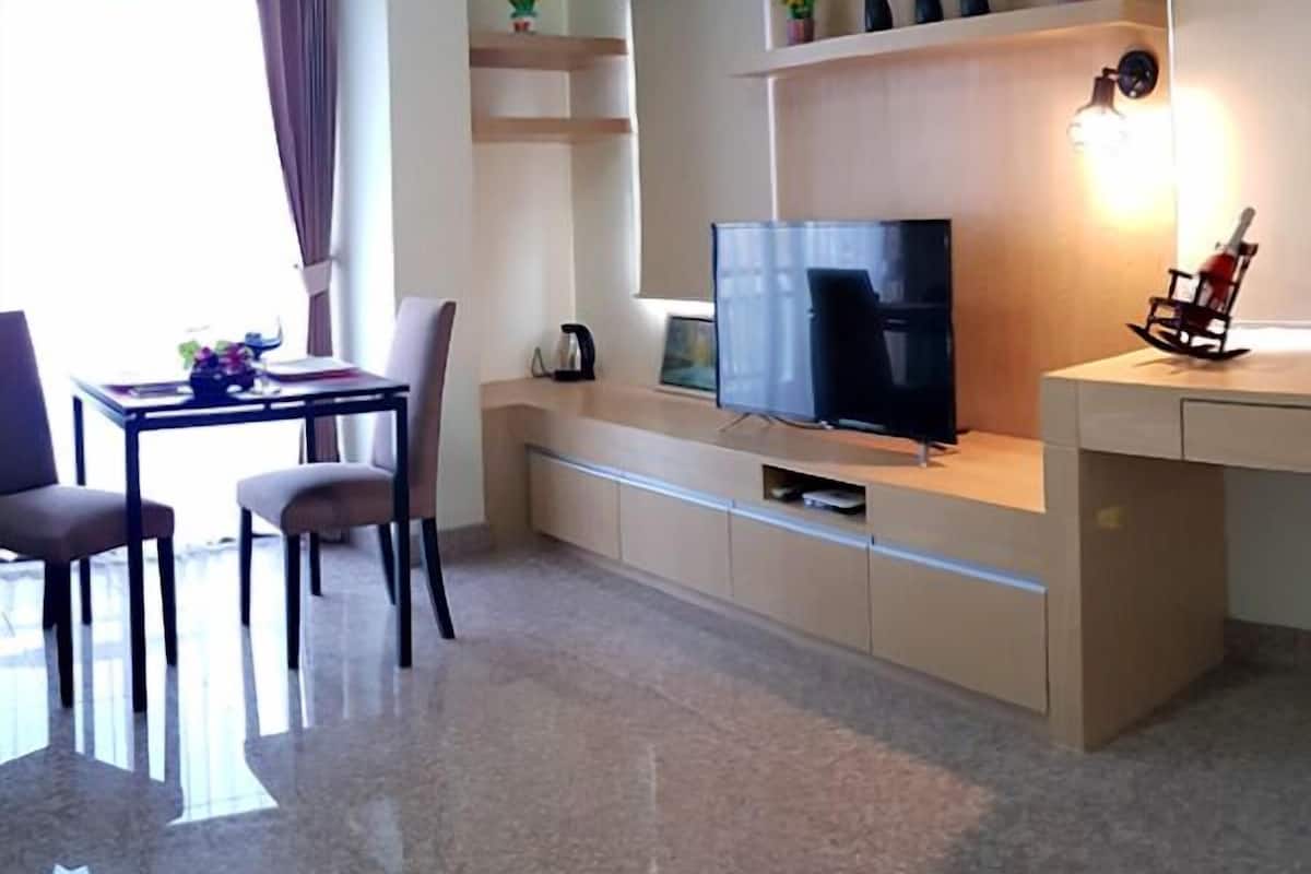 A modern living room with a flat-screen TV, a dining area with a table and chairs, and a kitchen area with a microwave and a coffee maker.