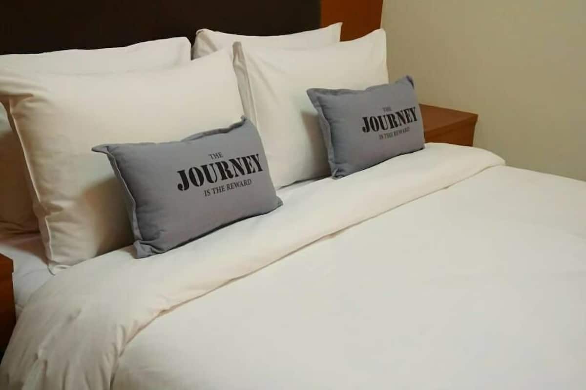 A neatly made bed with white bedding and two grey pillows with text.