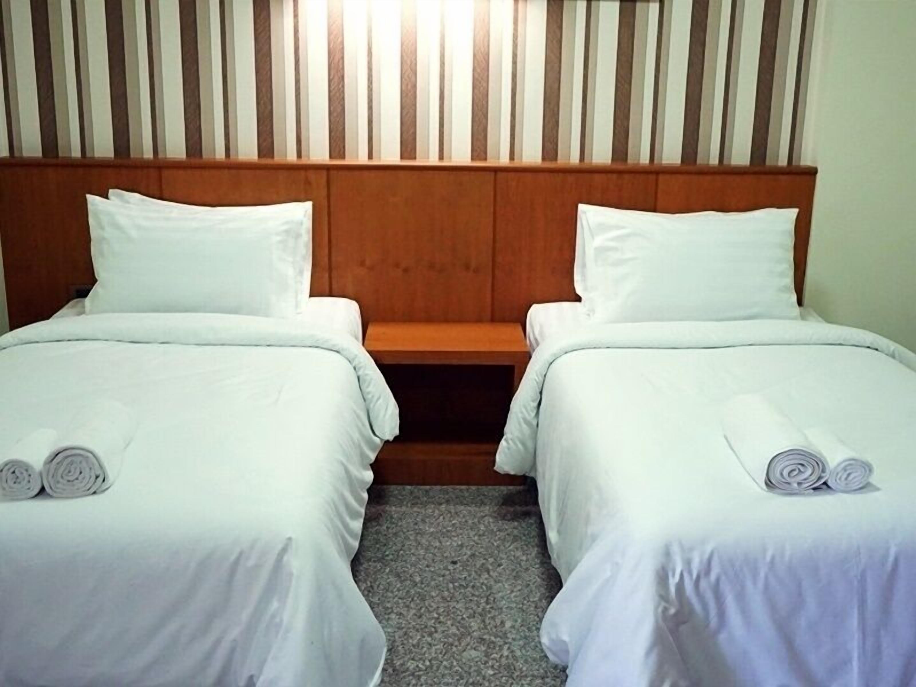 Quarto de hotel com duas camas de solteiro, cada uma com lençóis e almofadas brancas, e cabeceira de madeira.
