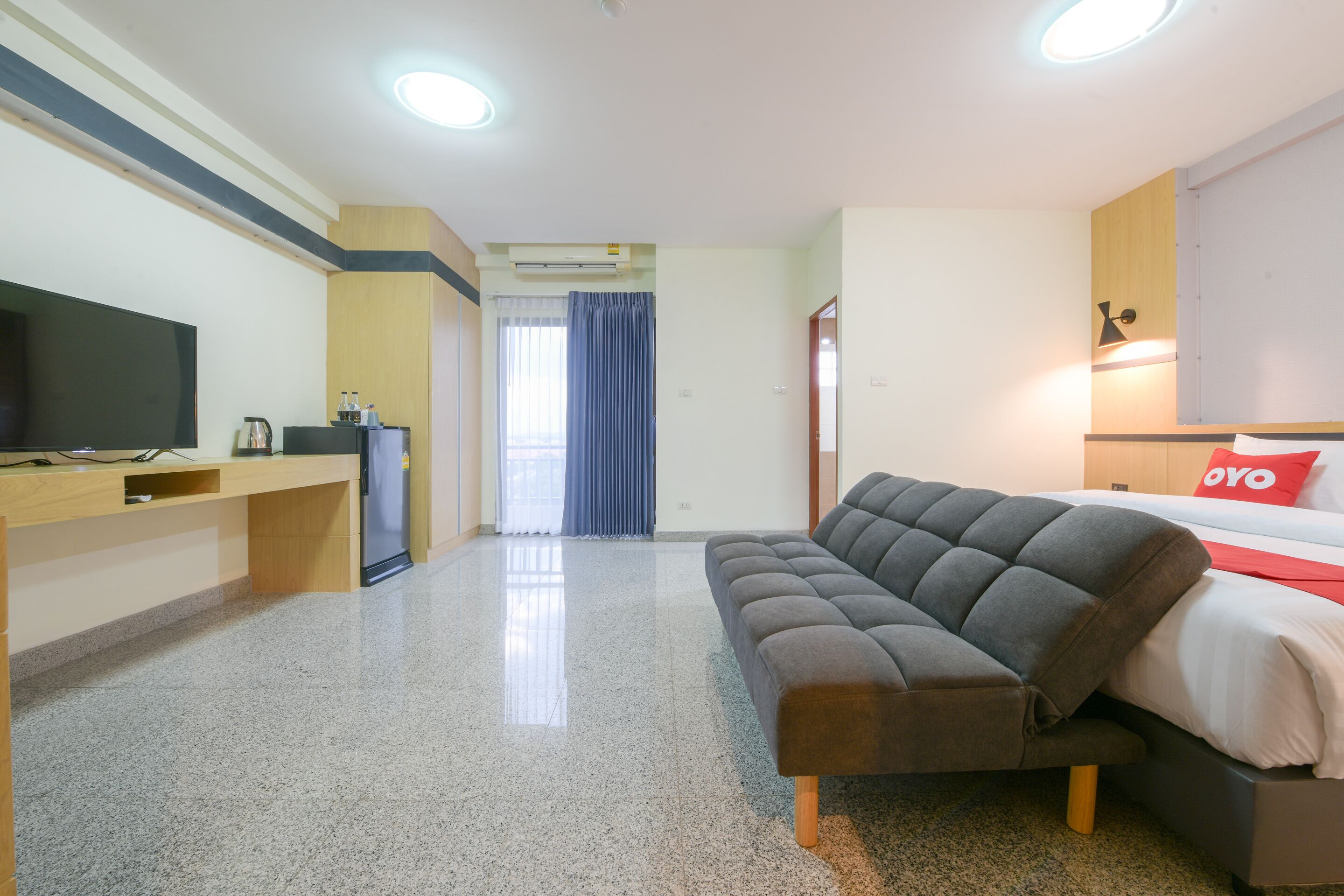 A modern hotel room with a sofa, a bed, a TV, and a desk.