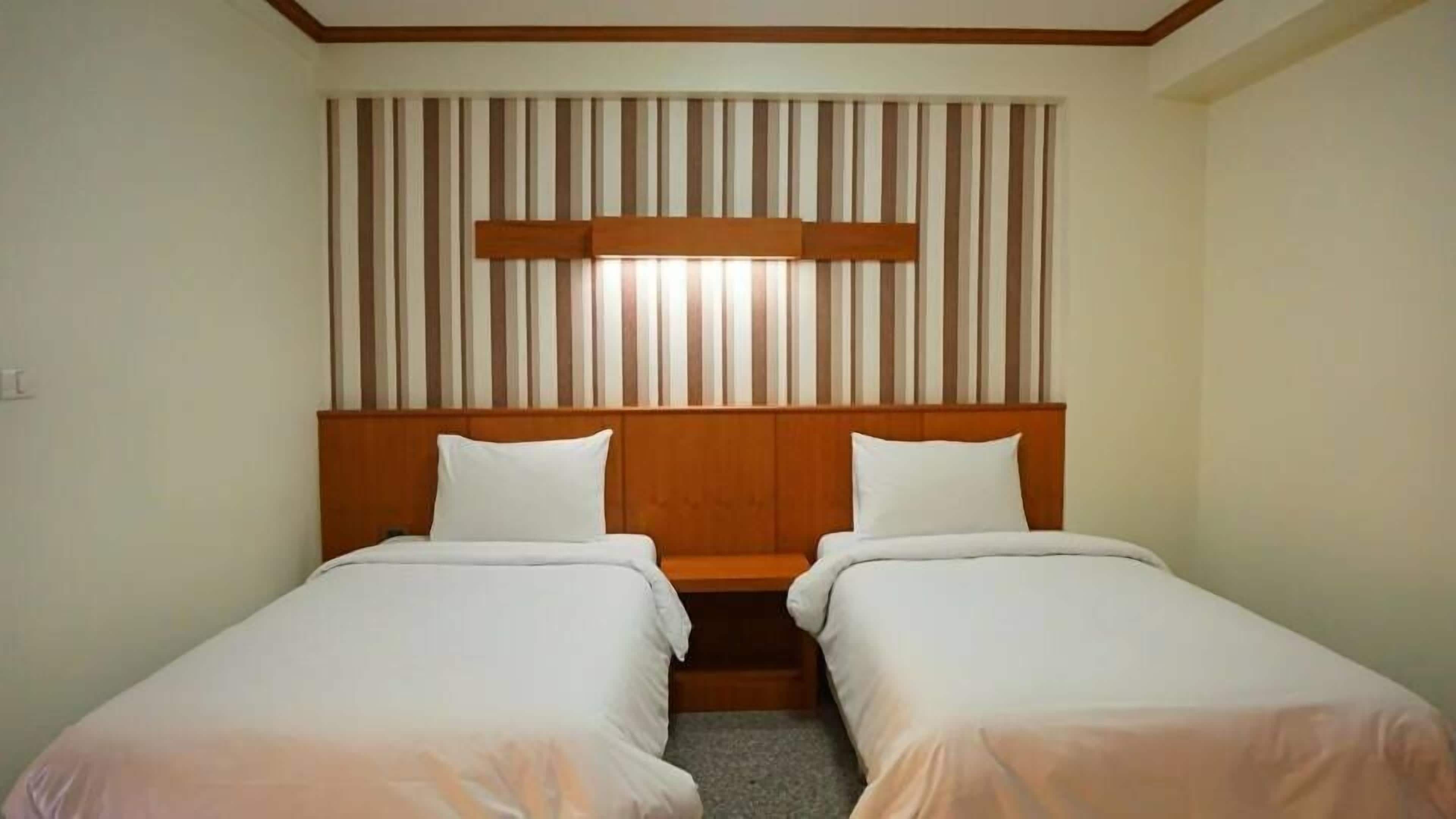 Una habitació d'hotel amb dos llits individuals, ambres a la fusta i una pantalla decorativa amb ratlles penjada sobre els llits.