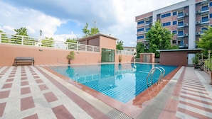 A swimming pool with a tiled deck, a small building with a door, and a multi-story residential building in the background. - The Route Sriracha Hotel And Residence (Si Racha)