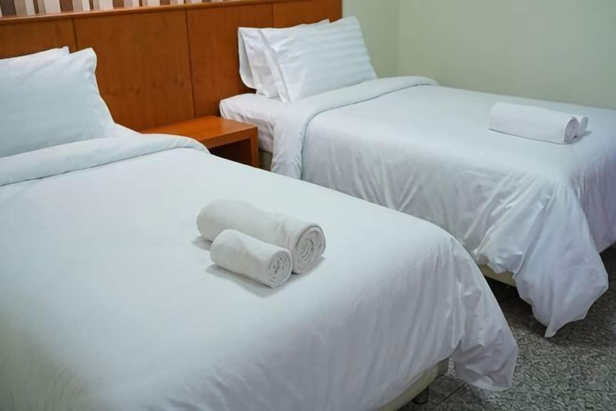 A hotel room with two single beds, each with white linens and pillows, a wooden headboard, and a small bedside table.