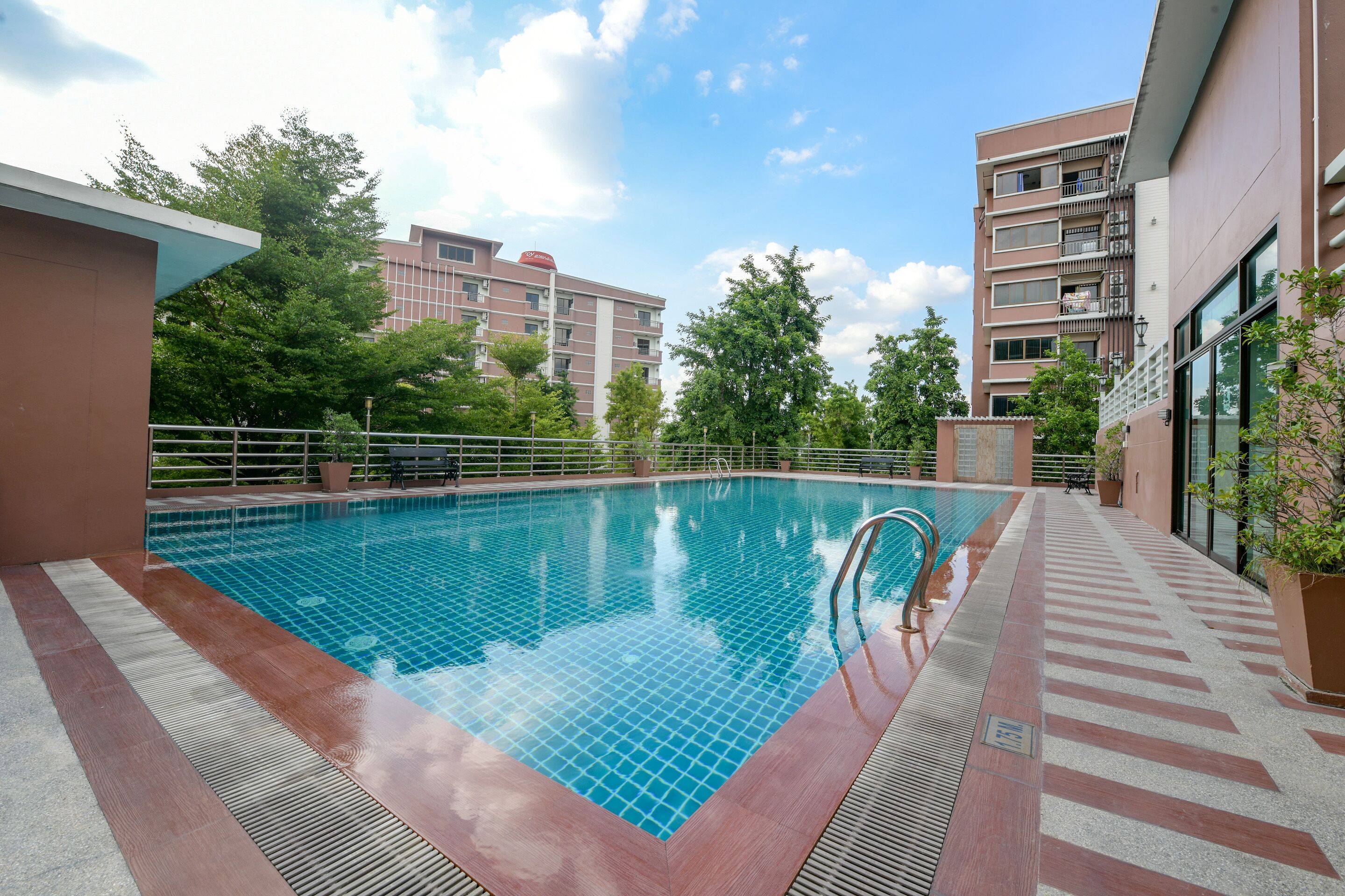 Une piscine dotée d’une terrasse carrelée, entourée d’immeubles et d’arbres.