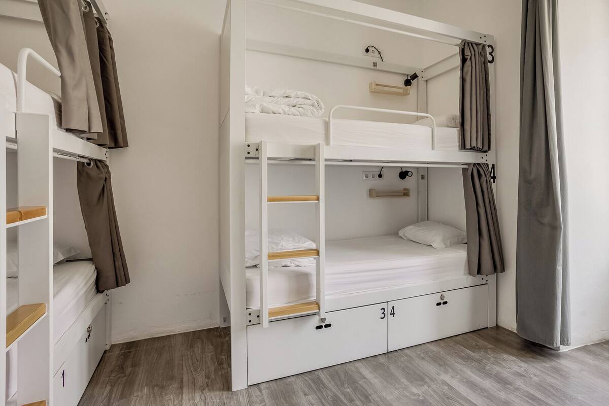 Une chambre avec un lit superposé, une armoire, une petite table et une fenêtre avec des rideaux.