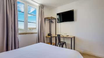 Habitación de hotel con cama, escritorio con silla, televisor montado en la pared y ventana con cortinas.