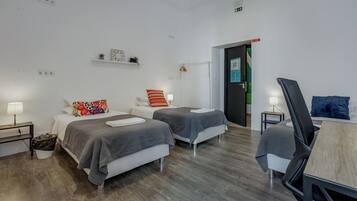 Een hotelkamer met twee bedden, een bureau, een stoel, een klein tafeltje en een prullenbak.