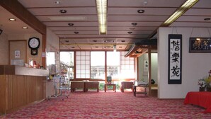 Um quarto japonês tradicional com piso de tatame, uma mesa de recepção de madeira, um relógio e vista através de amplas janelas.