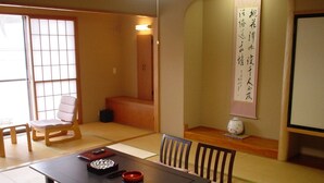 Um quarto japonês tradicional com tatames, uma mesa baixa com um recipiente vermelho e preto, e uma cadeira de madeira.