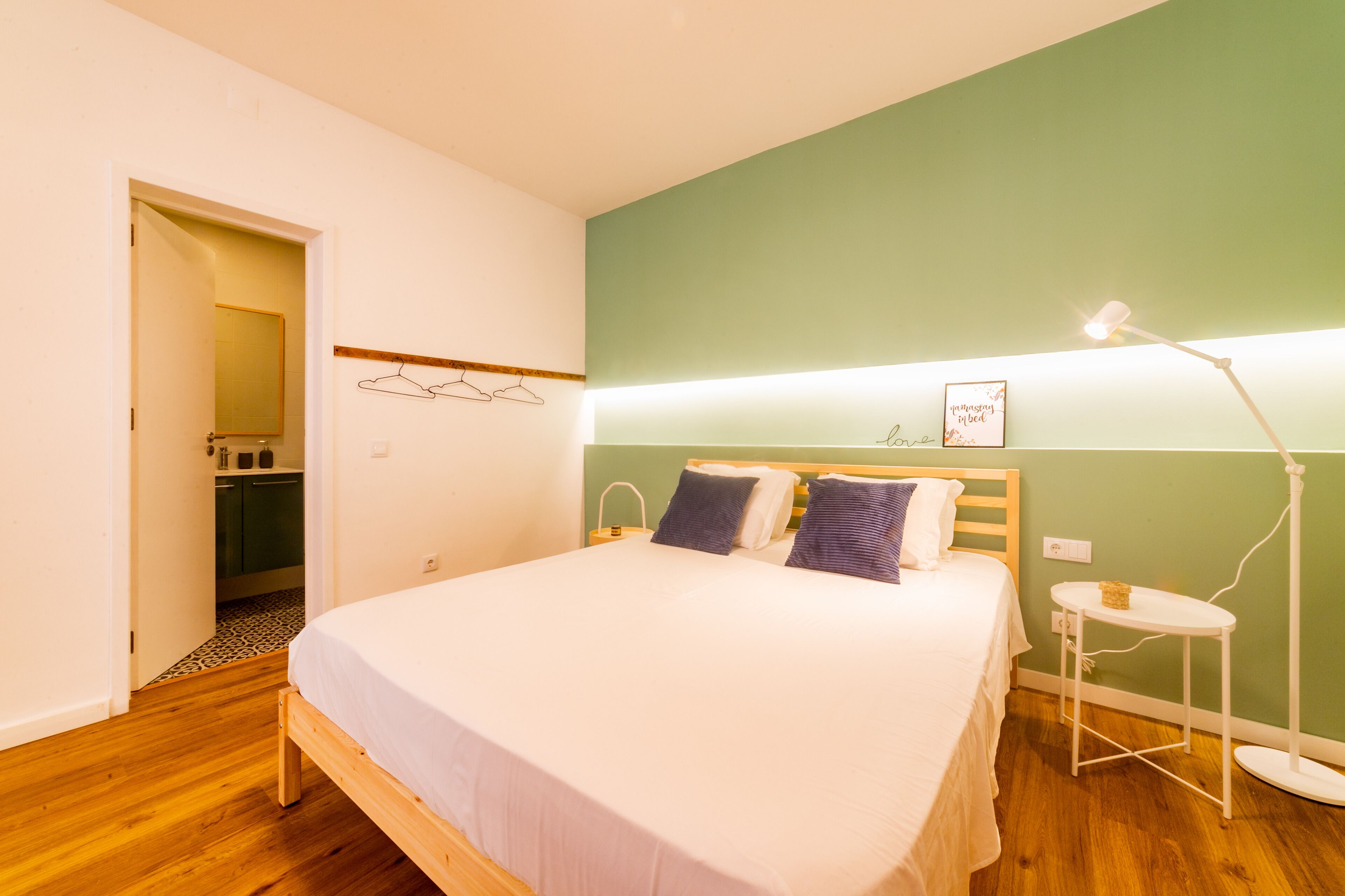 A bedroom with a bed, bedside table, lamp, and a wall-mounted shelf with a picture.