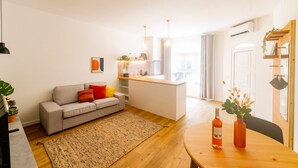 A modern living room with a grey sofa, a wooden dining table, and a kitchen area in the background.