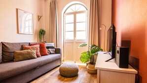 A cozy living room with a sofa, ottoman, potted plants, and a television on a stand.