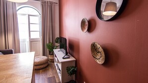 A room with a wooden dining table, a TV on a stand, a mirror on the wall, and a potted plant.