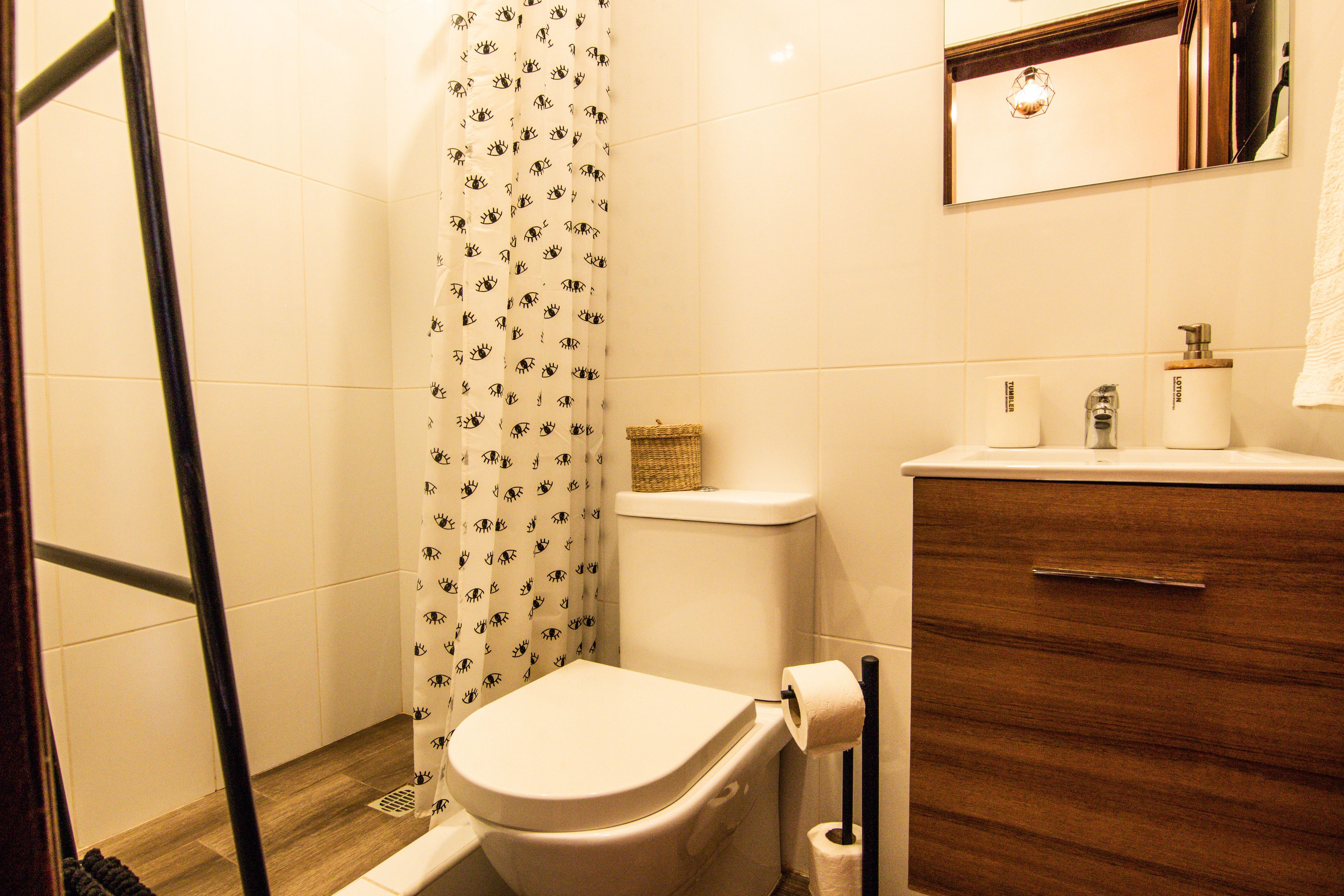 A bathroom with a toilet, a shower curtain, a wooden cabinet, and a mirror.