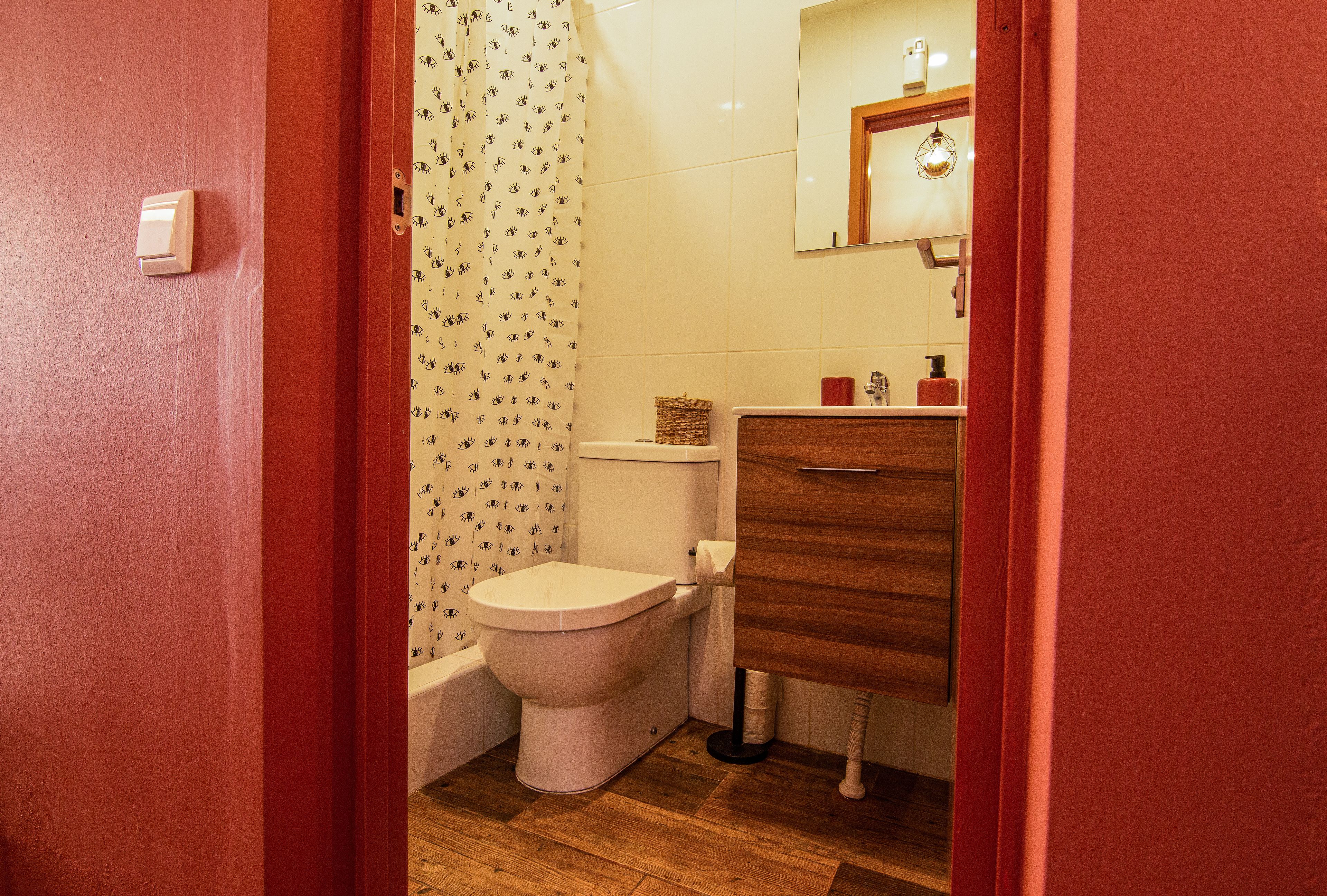 Une salle de bain comprenant des toilettes, un meuble en bois, un miroir et un rideau de douche à motifs floraux.