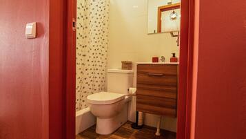 Une salle de bain comprenant des toilettes, un meuble en bois, un miroir et un rideau de douche à motifs floraux.