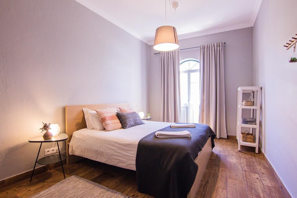 Un dormitorio con cama, mesita de noche, lámpara y una estantería con objetos.