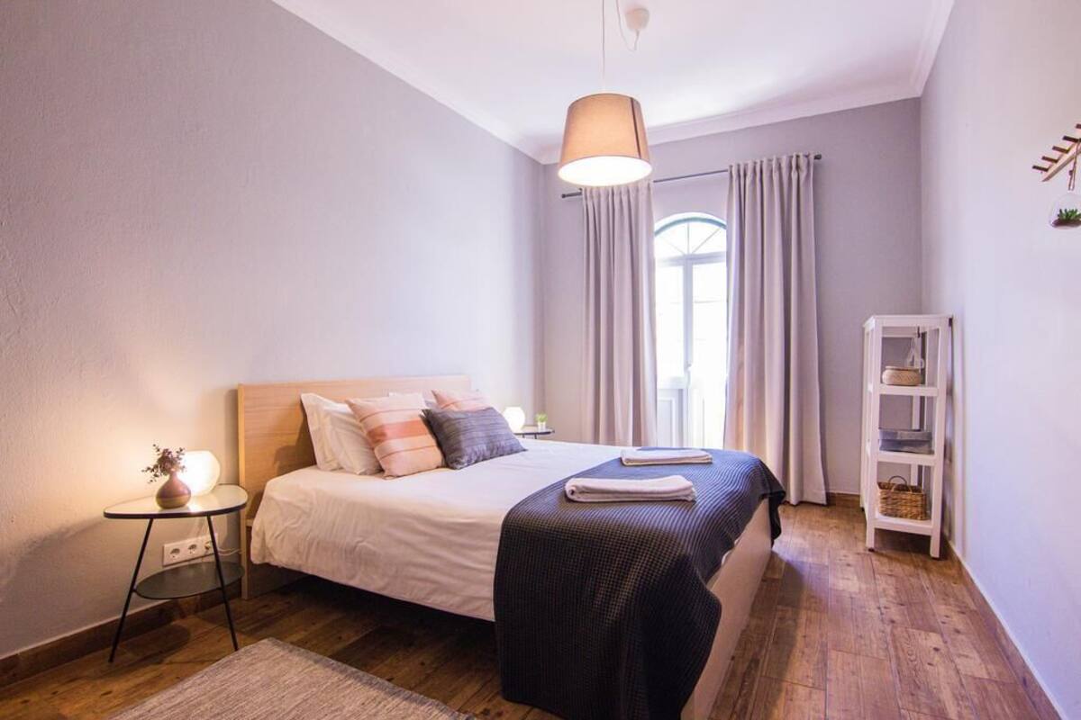 Une chambre à coucher avec un lit, une table de chevet, une lampe et une étagère sur laquelle sont posés divers objets.