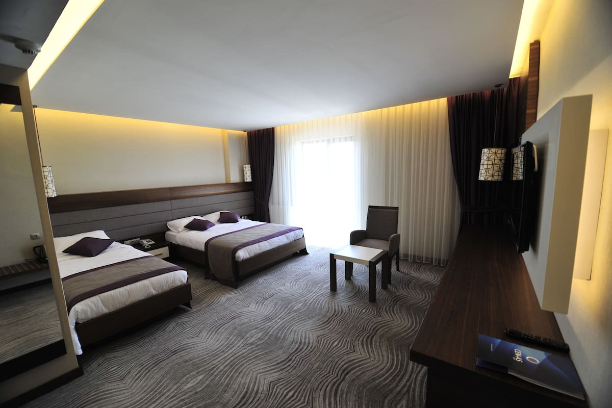 A hotel room with two beds, a desk, a chair, and a TV.