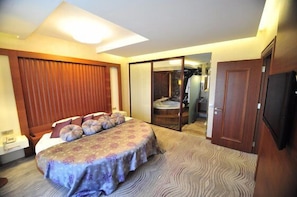 Une chambre d’hôtel avec un grand lit, une télévision, une porte coulissante donnant accès à la salle de bain et une armoire en bois.
