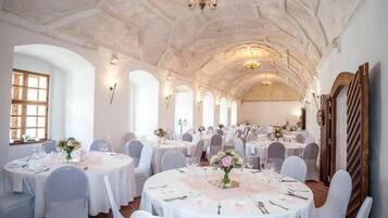 Un salón de banquetes con mesas redondas dispuestas para cenar, techos abovedados y candelabros.