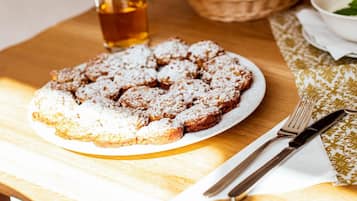 A plate of pastries dusted with powdered sugar on a wooden table with a glass of tea and cutlery.