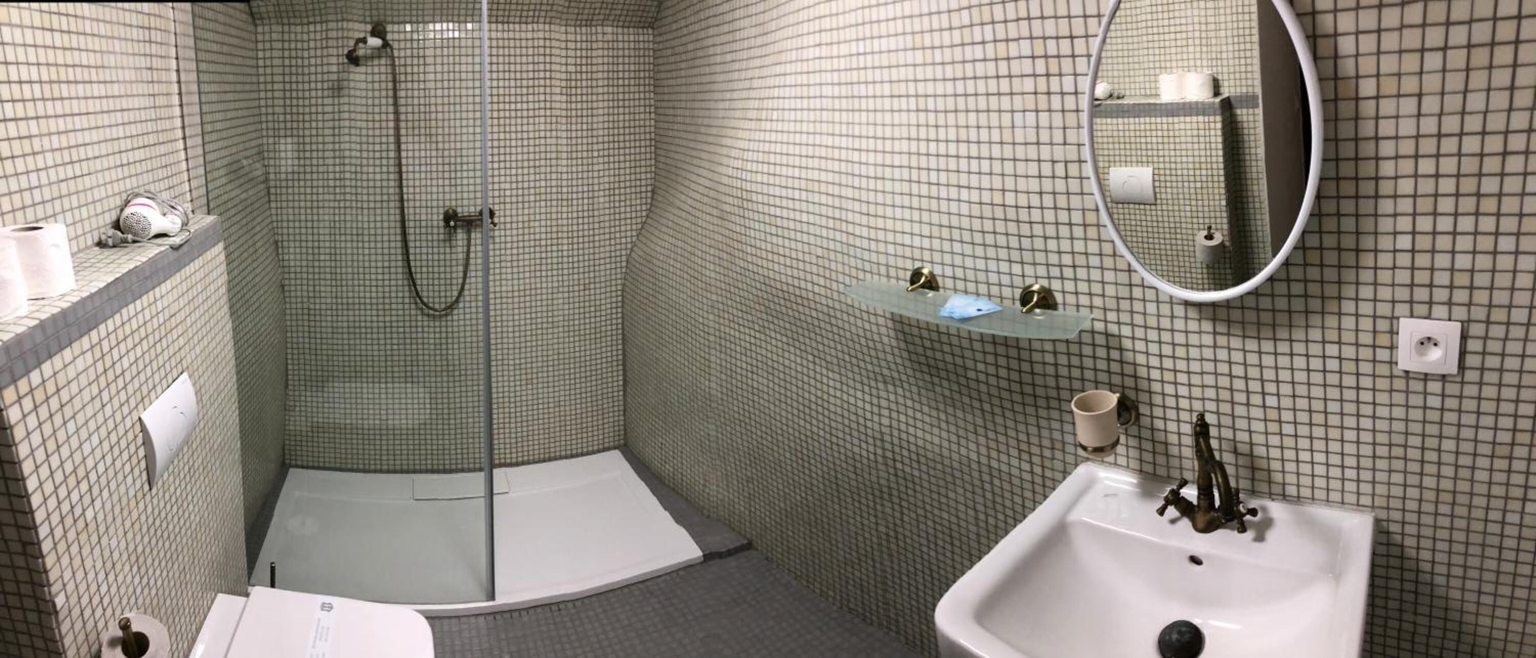 Un baño en esquina con ducha, lavamanos y espejo.