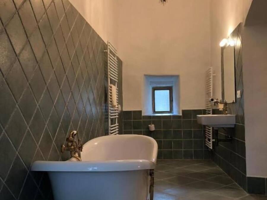 A bathroom with a freestanding bathtub, a chandelier, a window, and a mirror.