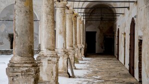 Un pasillo con columnas y arcos de piedra que conduce a un vano oscuro.