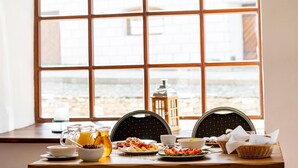Una mesa de desayuno con varios platos, una jarra de jugo de naranja y un farol en una habitación con ventanas amplias.
