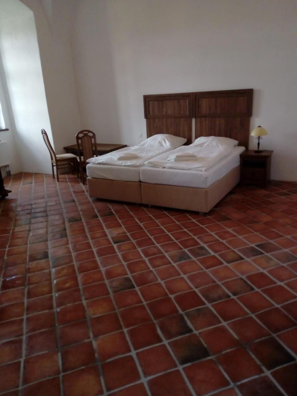 Ein Zimmer mit Bett, Stuhl, Tisch und Lampe.