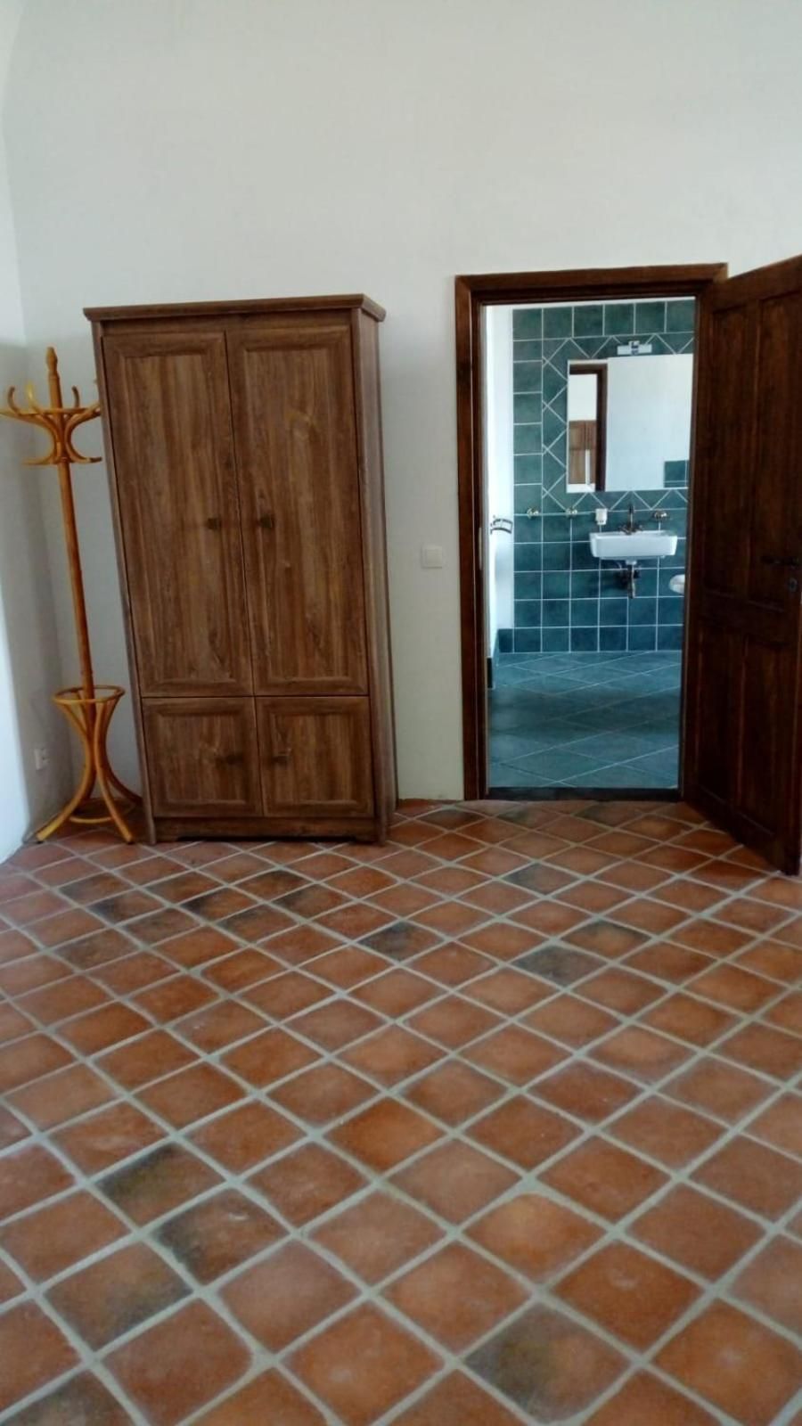 Une pièce dotée d’un sol carrelé, d’une armoire en bois et d’un passage menant à une salle de bain avec un lavabo et des murs carrelés.