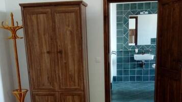 Une pièce dotée d’un sol carrelé, d’une armoire en bois et d’un passage menant à une salle de bain avec un lavabo et des murs carrelés.