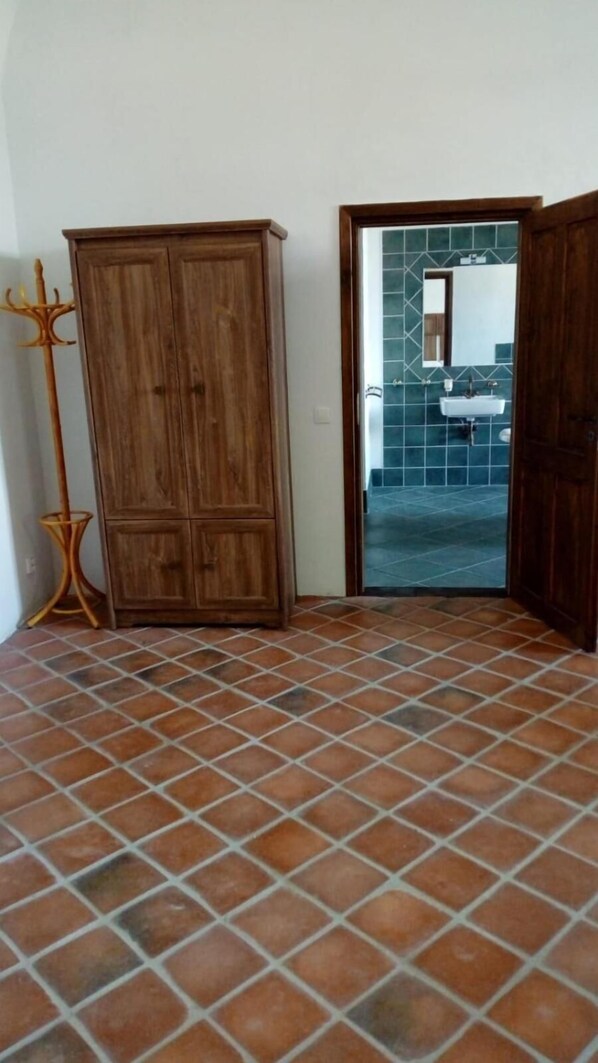 A room with a tiled floor, a wooden wardrobe, and a doorway leading to a bathroom with a sink and tiled walls. - Chateau Goldenstein (Branna)