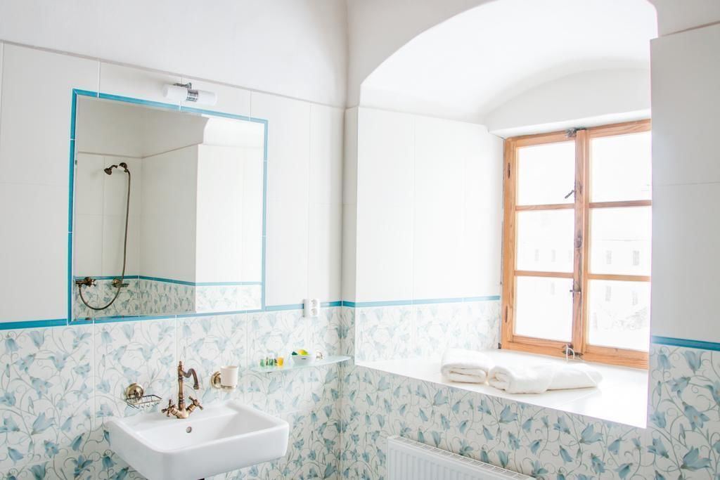 Un baño con un lavamanos blanco, un espejo, una ducha y una ventana con marco de madera.