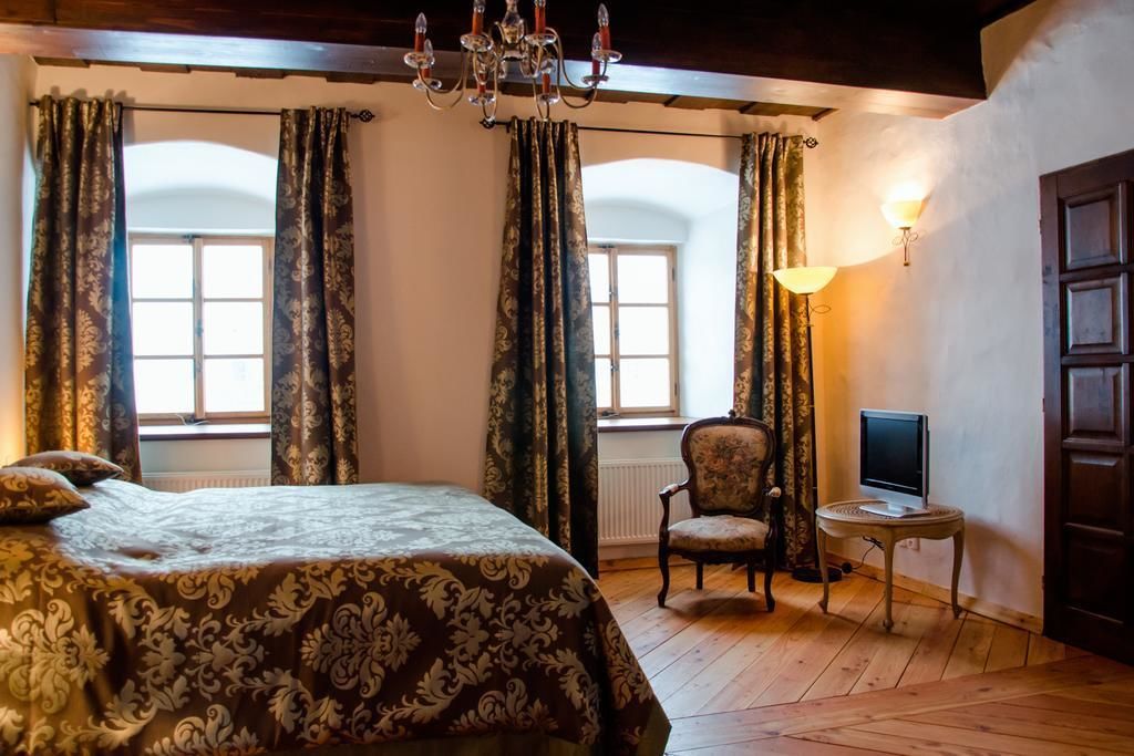 A bedroom with a large bed, a chair, a small table with a TV, and a chandelier.