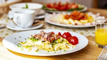 A breakfast setting with plates of food, cups, and a glass of orange juice on a table.