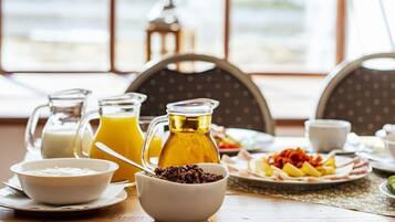 Un desayuno con una mesa, una jarra de jugo de naranja, un tazón de cereal y un plato de fruta y tocino.