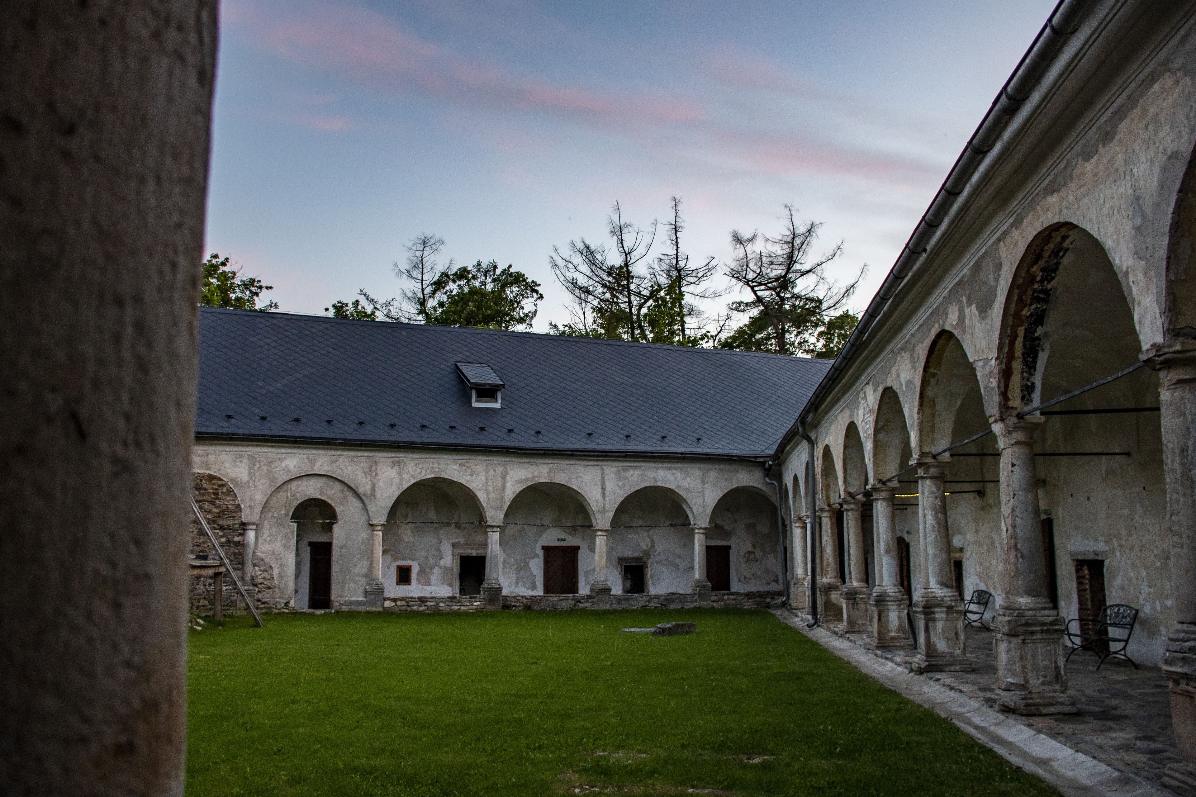 A courtyard with a building featuring arched walkways and a grassy area.