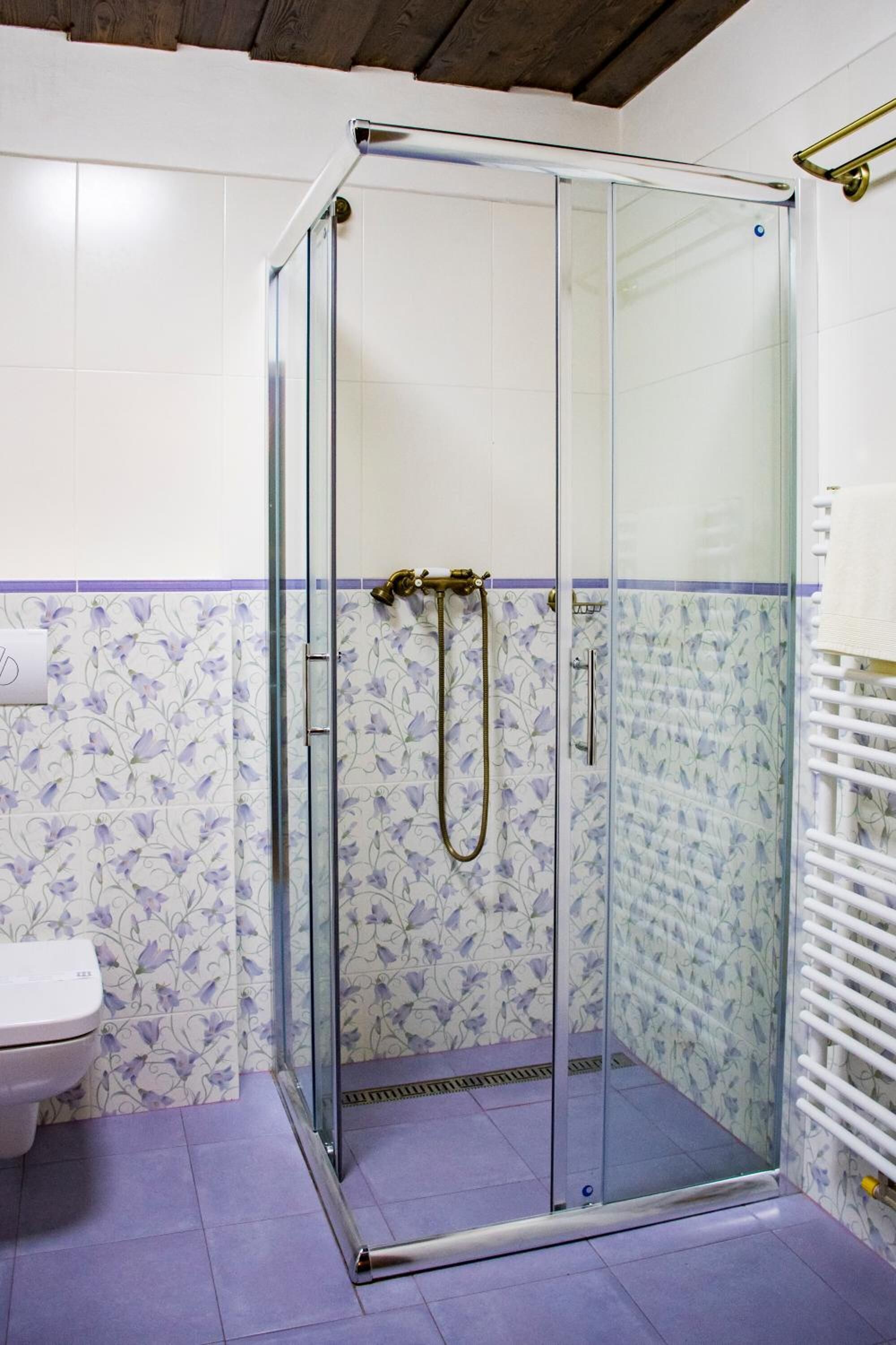 Una ducha con puerta de vidrio, un inodoro blanco y una pared de azulejos con diseño floral.