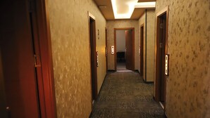 Un corridoio d'albergo con pavimenti in moquette, porte in legno e luci a parete.