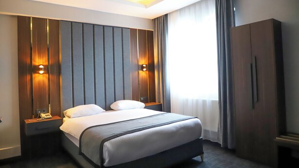 Una camera d'albergo moderna con un letto grande, comodini, un armadio e una finestra con tende.