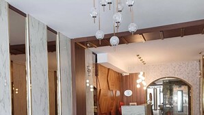 Una hall d'albergo con la reception, un'area salotto con poltrone, un pavimento decorato e un lampadario ornamentale.