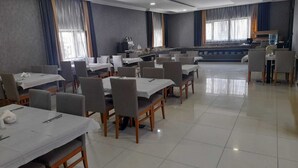 Spaziosa zona pranzo con diversi tavoli e sedie, angolo cottura sullo sfondo e ampie finestre con tende.