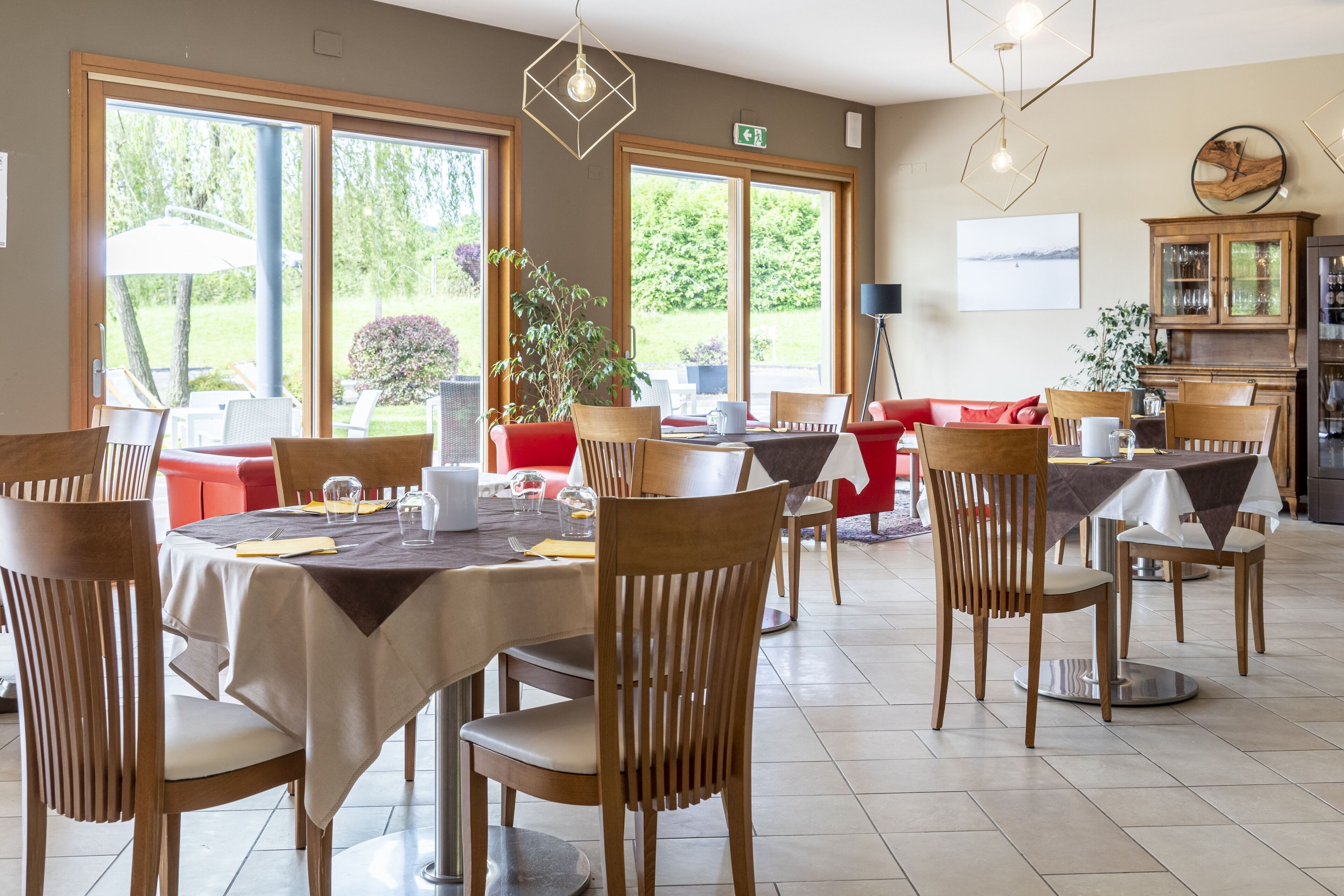 A dining area with round tables, wooden chairs, and a red sofa.