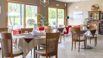 A dining area with round tables, wooden chairs, and a red sofa.