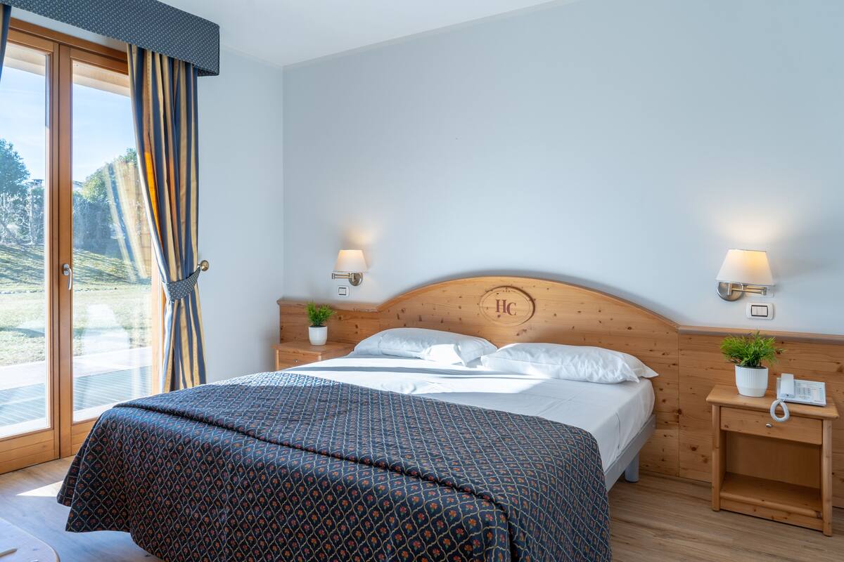 A bedroom with a large bed, wooden headboard, bedside tables with lamps, and a view through a glass door.