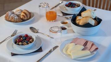 Una mesa de desayuno con cruasanes, un bol de bayas, un vaso de zumo de naranja y un plato de jamón y queso.