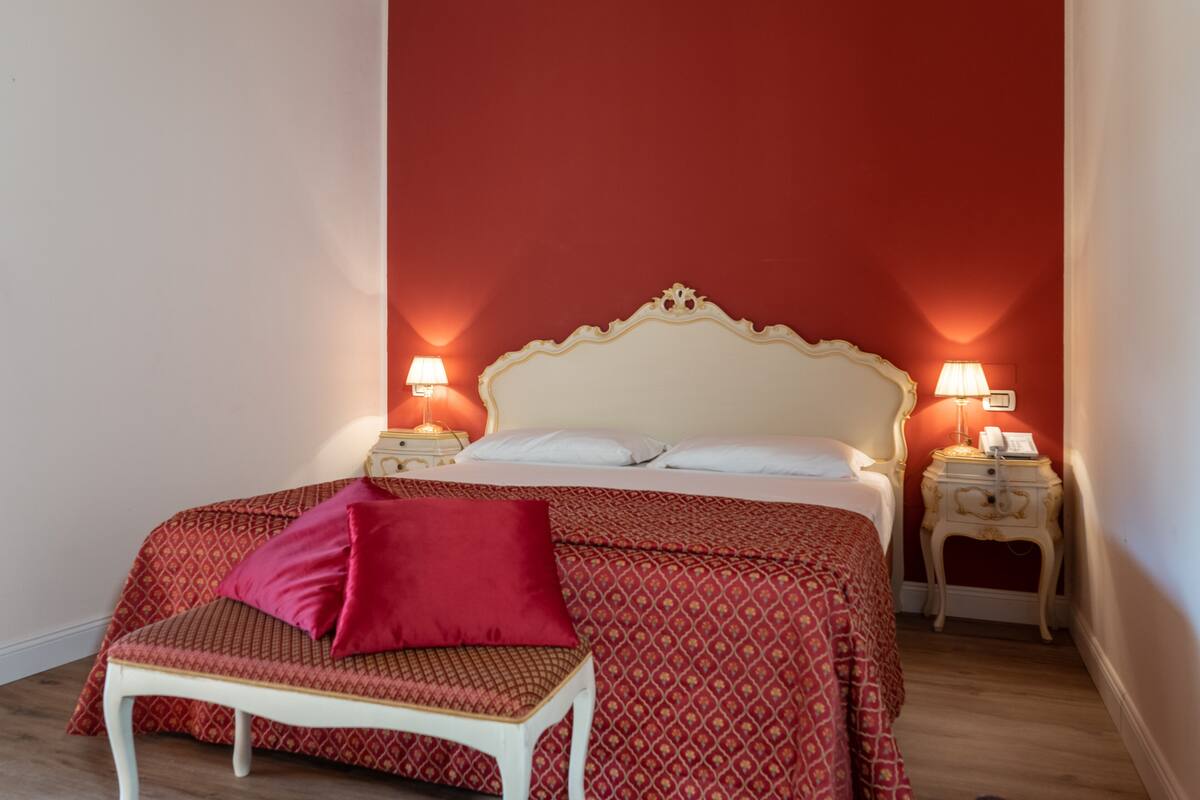A bedroom with a large bed, two bedside tables, a chair, and a red wall.